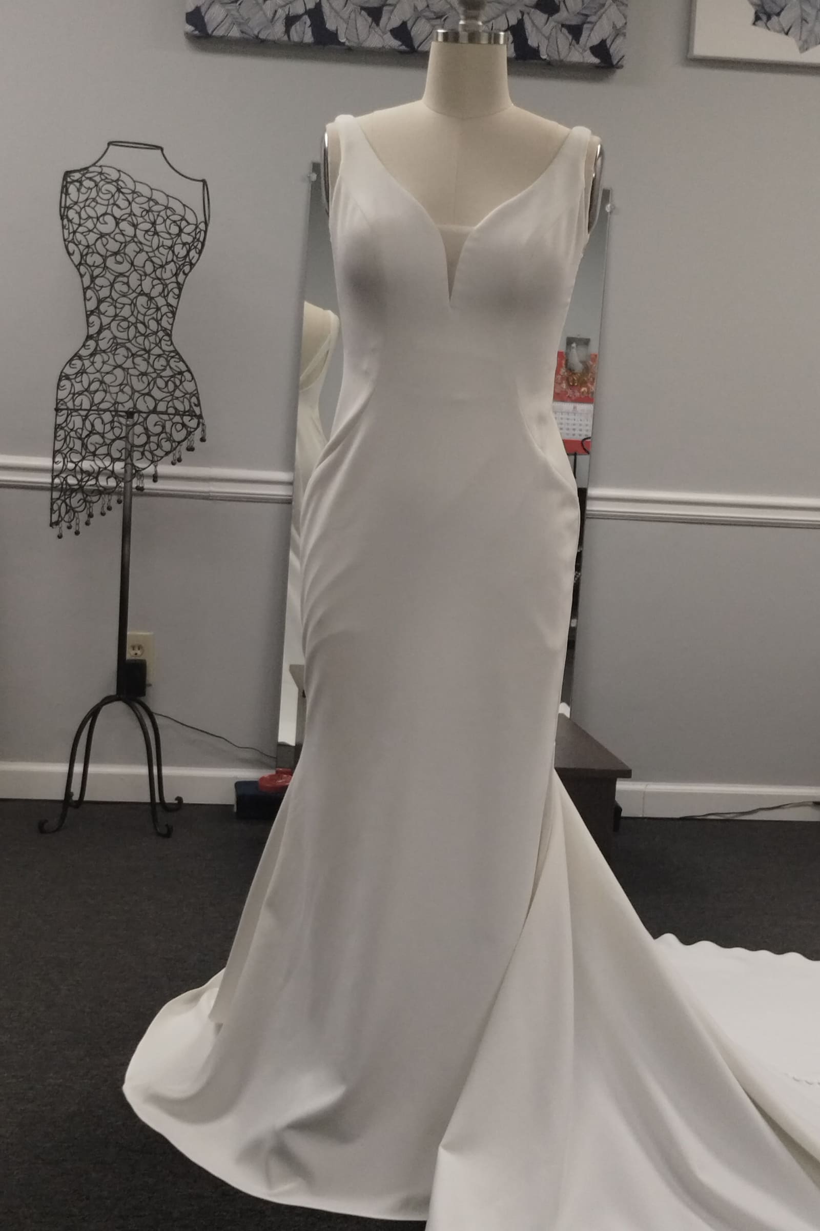 Ivory crepe mermaid wedding dress with a long train on a dress form