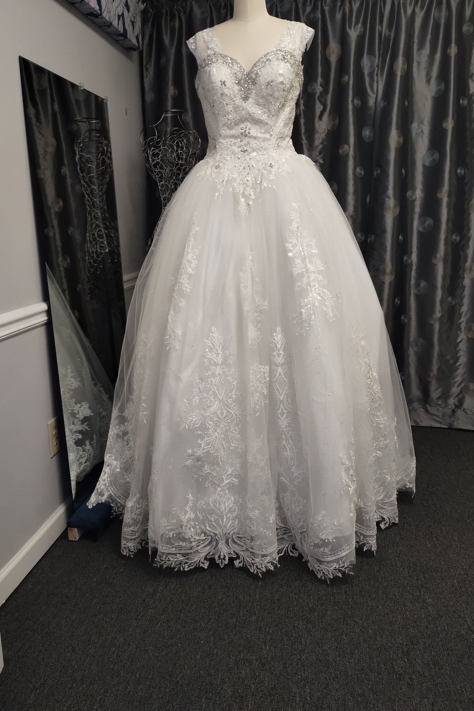 White lace ball gown with a scalloped hem on a dress form in the atelier